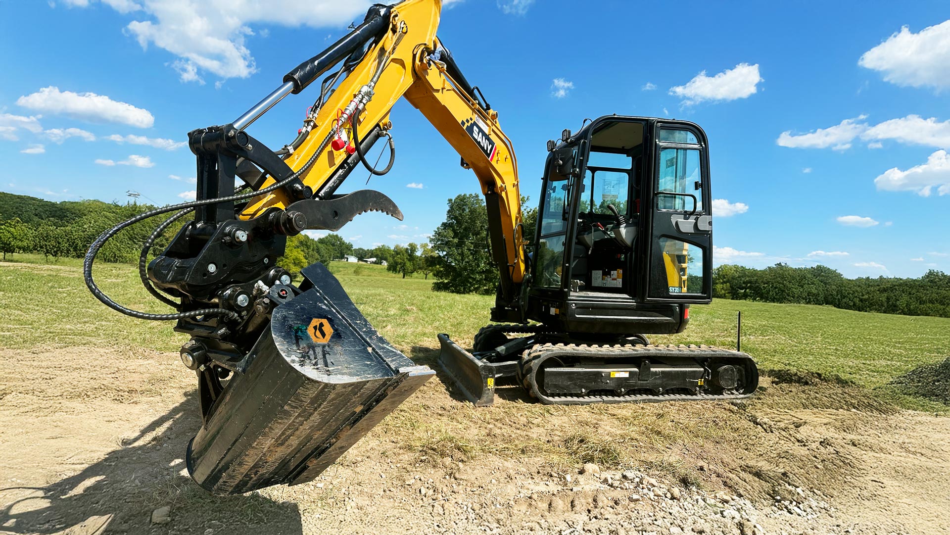 A mini excavator digging with a tilt bucket and a thumb attached with a coupler.