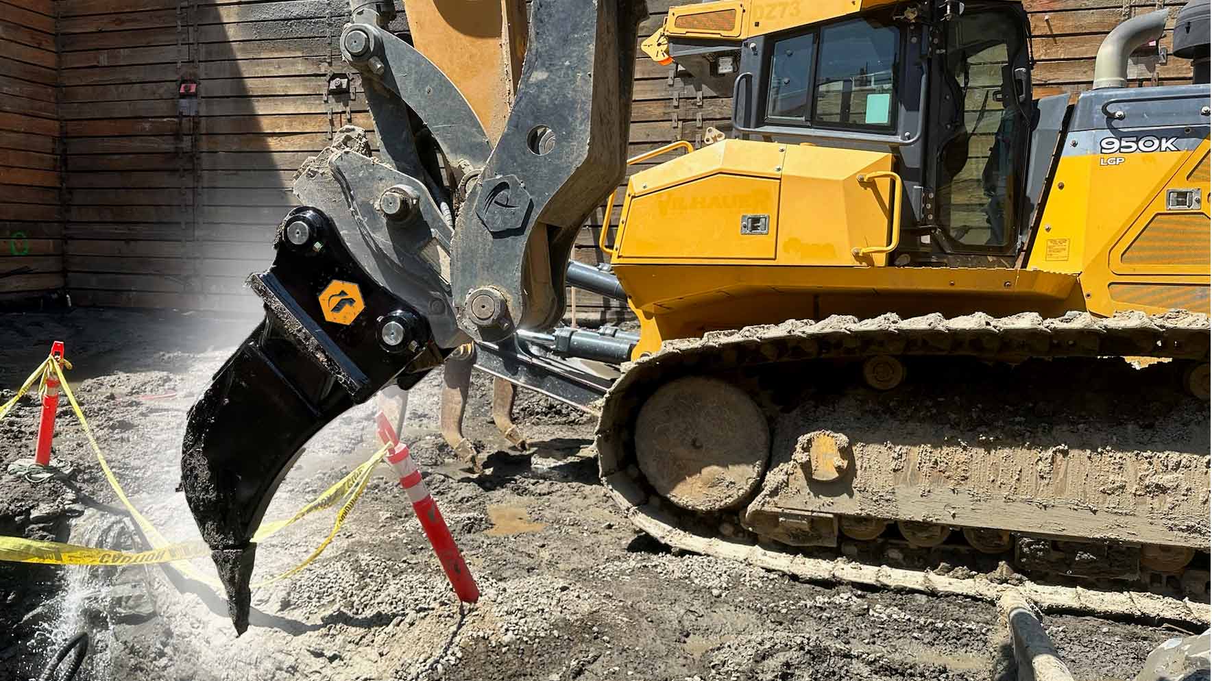 An excavator digging at a construction site with a ripper and a thumb attachment.