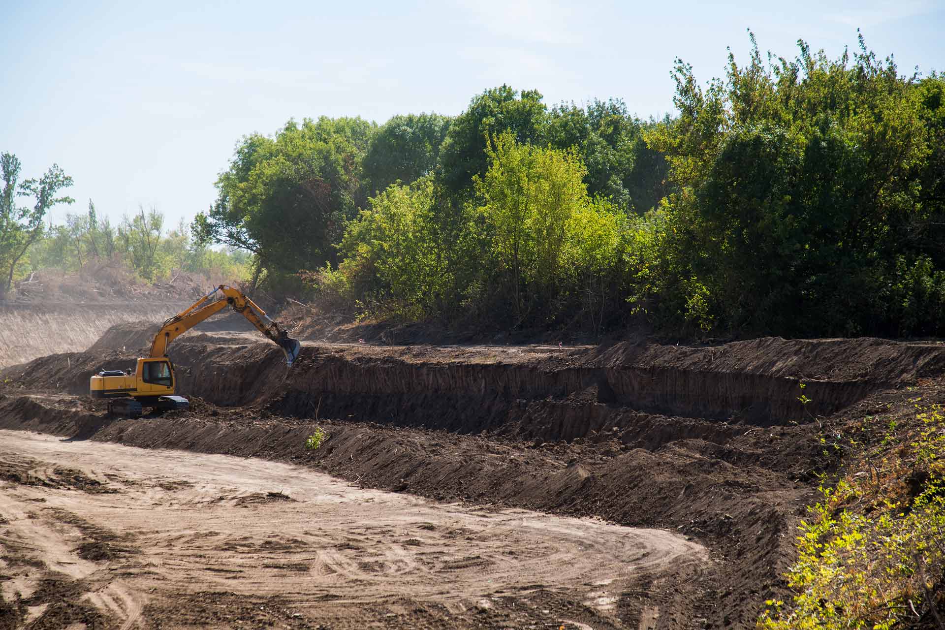 An excavator digs dirt in a wooded rural setting.