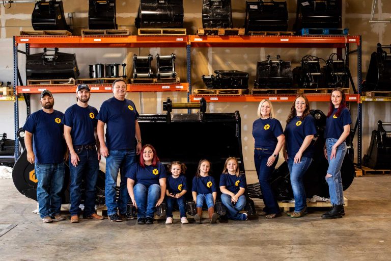 The TRUE Attachments team in their Springfield Missouri warehouse surrounded by excavator attachments.